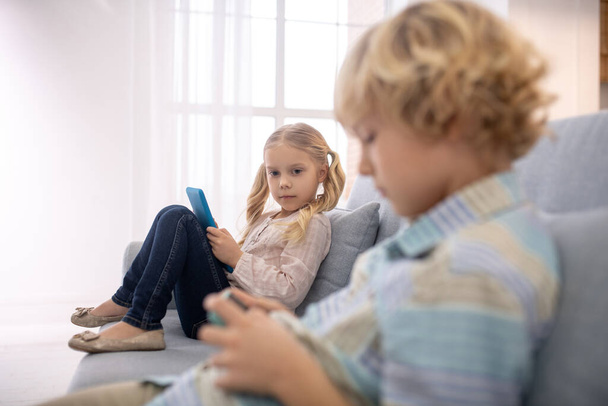Children sitting on sofa and playing with gadgets - Photo, Image
