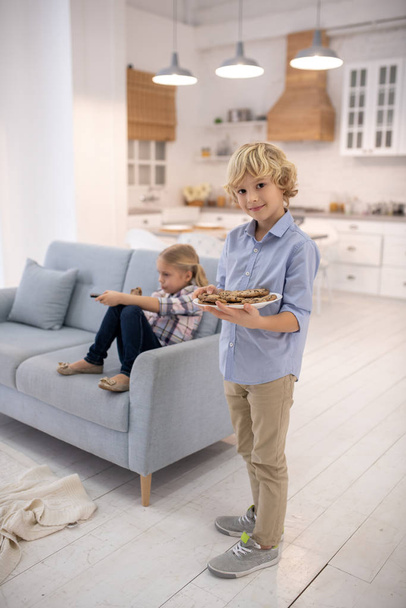 Boy with biscuits, girl sitting and switching channels - Photo, Image