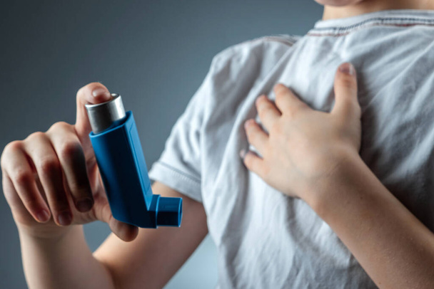 The boy holds an asthma inhaler in his hands to treat inflammatory diseases, shortness of breath. The concept of treatment for cough, allergies, respiratory tract disease. - Fotó, kép