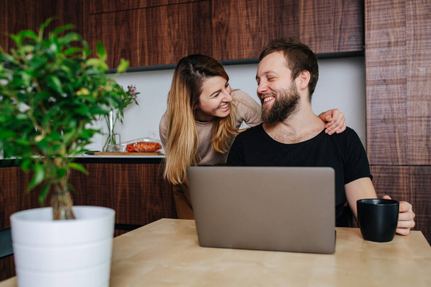 Man doing freelance work at the dining table and laughing with his girlfrend - Photo, Image