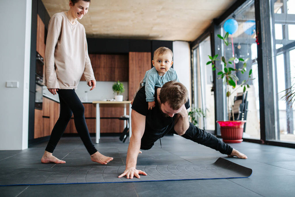 Father entertaining his baby while doing single arm plank - Fotoğraf, Görsel