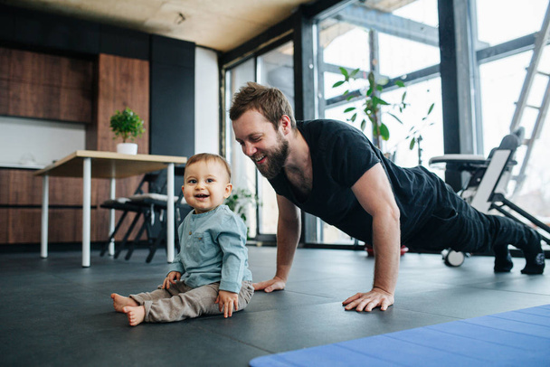 Man working out next to his infant baby, moved and amused by him. - Foto, Imagem