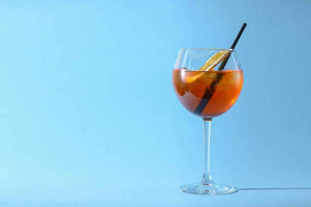 A glass of fruit liqueur in wine glass with a piece of lemon and black plastic straw isolated on pastel blue background. - 写真・画像