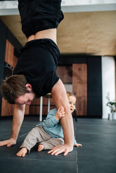 Father exercising, stadning on his hands next to his infant baby - Фото, зображення