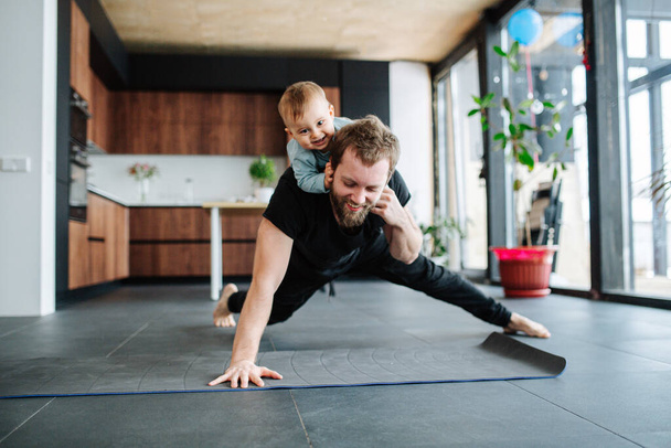Father working out, doing single arm plank with his jolly baby riding on him - Fotó, kép