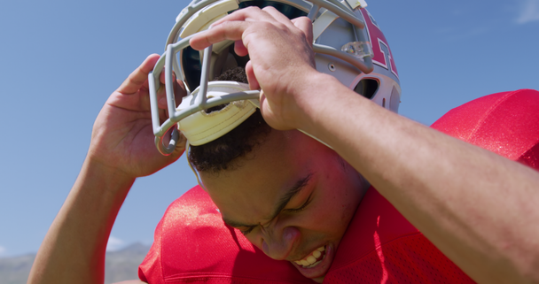 Side view close up of a mixed-raced American football player removing his helmet, against a blue sky at a sports field, in slow motion. Track and Field Sports Training in Stadium. - Séquence, vidéo