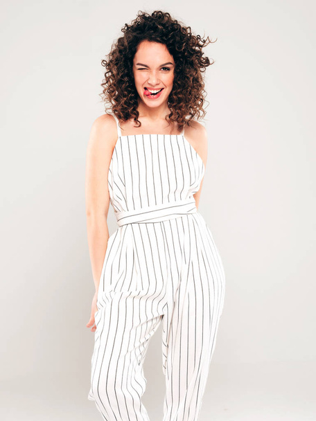 Portrait of beautiful smiling model with afro curls hairstyle dressed in summer hipster clothes.Sexy carefree girl posing in studio on gray background.Trendy funny and positive woman shows tongue - Photo, Image