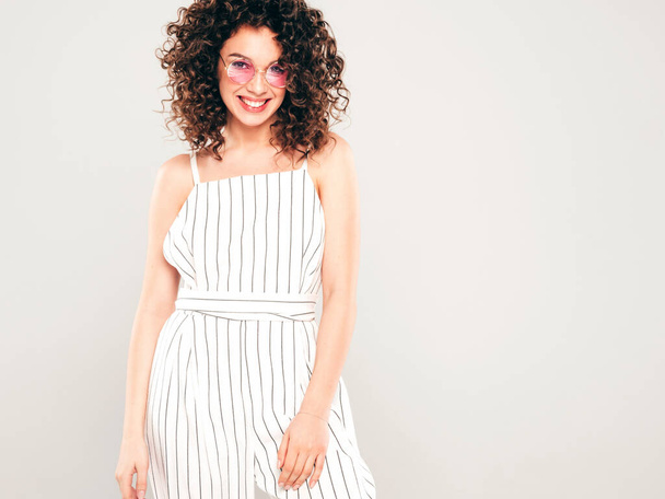 Portrait of beautiful smiling model with afro curls hairstyle dressed in summer hipster clothes.Sexy carefree girl posing in studio on gray background.Trendy funny and positive woman - Photo, image