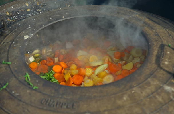 Medieval style cooking of various vegetables in big metal pot - Photo, Image