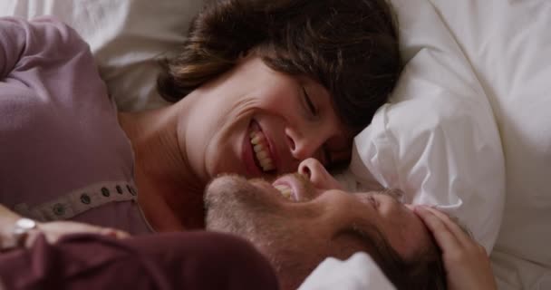 High angle side view of a Caucasian couple enjoying family time at home, laying in bed embracing, smiling, slow motion - Filmati, video