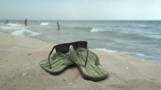 Tartozékok a strandon fekvő homok, férfi papucs és napszemüveg a strandon homok - Felvétel, videó