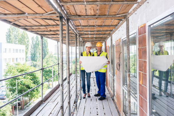 Construction worker and builder on scaffolding reading the plan - Φωτογραφία, εικόνα
