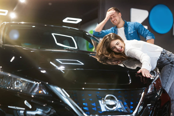 young couple handsome man and beautiful woman feeling happy and joyful buying their new vehicle in electric car dealership center - Фото, изображение
