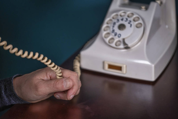 Τηλέφωνο παλιό ρετρό, ντεμοντέ λευκό τηλέφωνο σε πράσινο φόντο, γυναίκα χέρι κρατώντας καλώδιο τηλεφώνου - Φωτογραφία, εικόνα