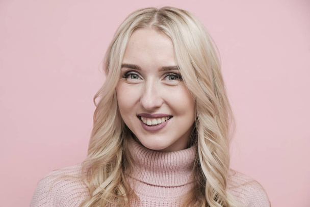 Happy woman face with blond hair in wool sweater on pastel pink background. Close up - Foto, afbeelding