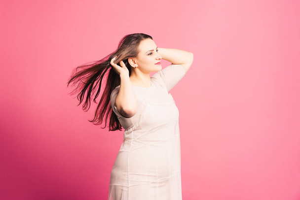 Plus size model with long hair blowing in the wind, fat woman on pink background - Фото, зображення