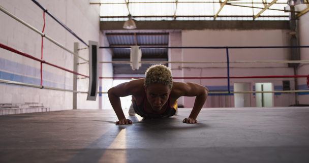 Front view of a mixed race female boxer with short curly hair wearing a vest and boxing shorts at a boxing gym, doing press ups in a boxing ring, slow motion - Filmmaterial, Video