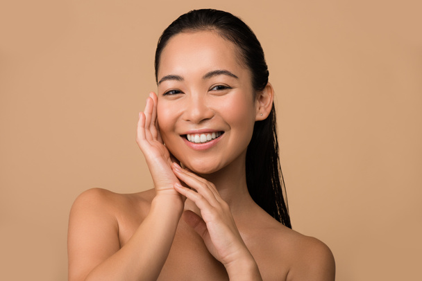 smiling beautiful naked asian girl touching face isolated on beige - Photo, Image