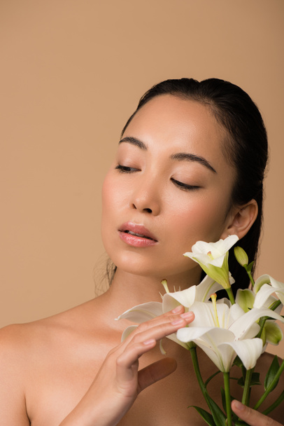 beautiful naked asian girl with white lilies looking away isolated on beige - Foto, immagini