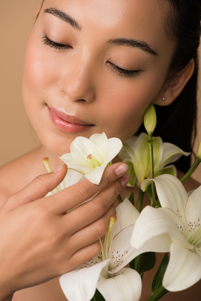 smiling beautiful naked asian girl with closed eyes and white lilies isolated on beige - Photo, image