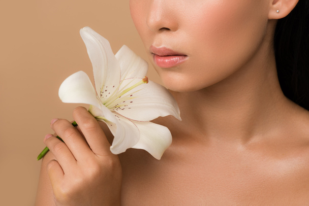cropped view of beautiful naked asian girl holding white lily isolated on beige - Foto, Imagen
