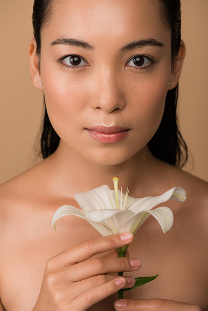 beautiful naked asian girl holding white lily isolated on beige - Фото, зображення