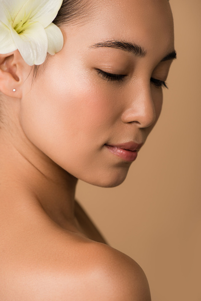 krásná nahá asijská dívka s bílou lilií ve vlasech izolovaných na béžové - Fotografie, Obrázek