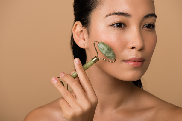 schön nackt asiatische Mädchen massieren Gesicht mit Jade-Rolle isoliert auf beige - Foto, Bild