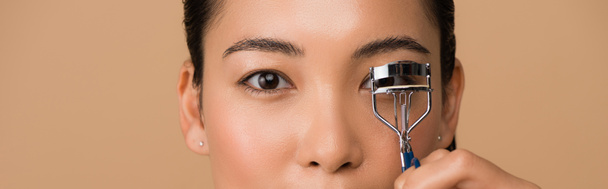 cropped view of beautiful asian girl using eyelash curlers isolated on beige, panoramic shot - Фото, зображення