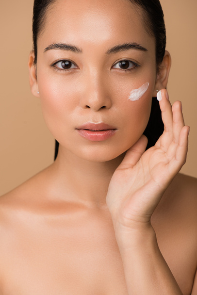 beautiful naked asian girl applying facial cream isolated on beige - Photo, Image