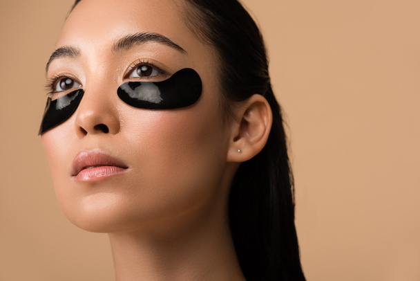 красивая азиатская девушка с черным гидрогелевым глазом повязки под глазами изолированы на бежевый
 - Фото, изображение