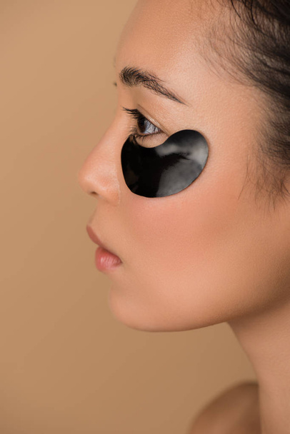 profile of beautiful asian girl with black hydrogel eye patch isolated on beige - Photo, Image