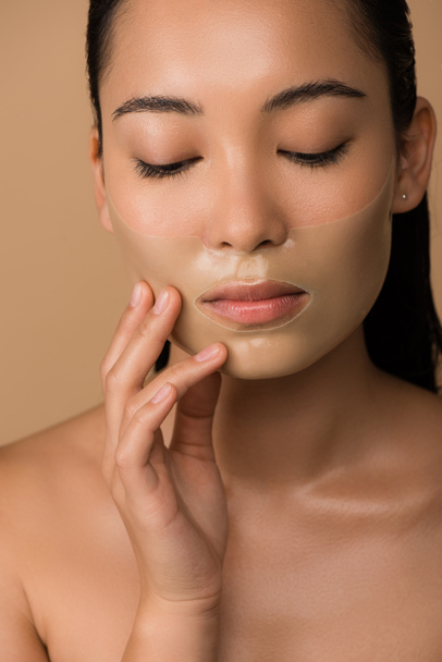 beautiful naked asian girl with closed eyes and hydrogel mask on face isolated on beige - Fotografie, Obrázek