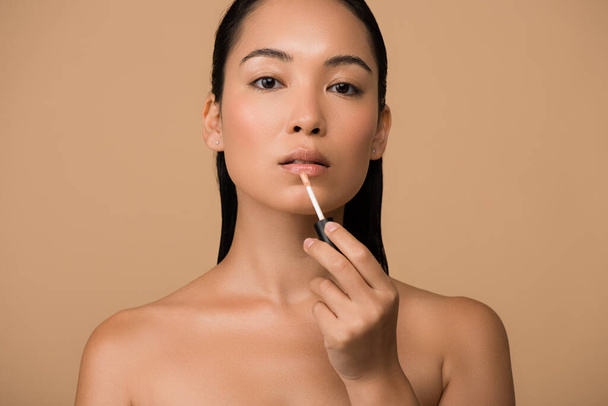 beautiful naked asian girl appying lip gloss on lips isolated on beige - Zdjęcie, obraz