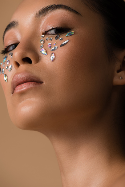 low angle view of beautiful asian girl with rhinestones on face isolated on beige - Foto, afbeelding
