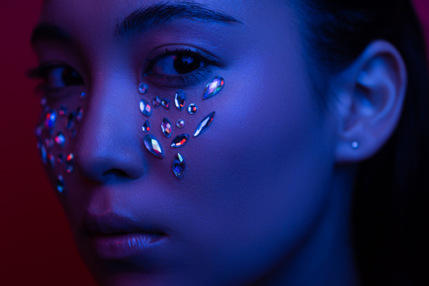 hermosa chica asiática con diamantes de imitación en la cara en luz azul
 - Foto, imagen