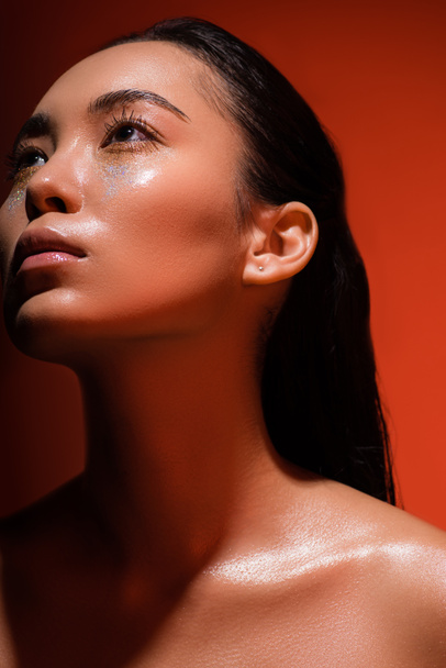 low angle view of beautiful naked asian girl with silver sparkles on face on red - Fotoğraf, Görsel