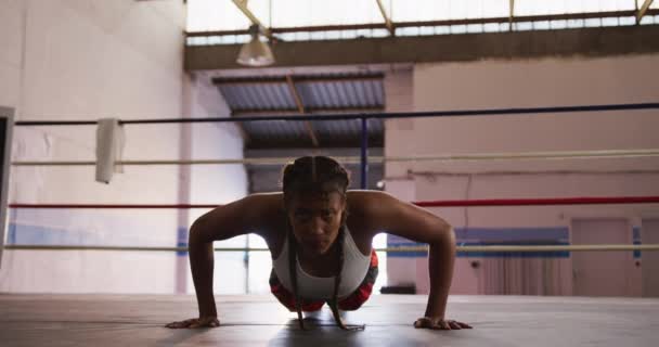 Front view of a mixed race female boxer with long plaited hair wearing a vest and boxing shorts at a boxing gym, doing press ups in a boxing ring, slow motion - Filmagem, Vídeo