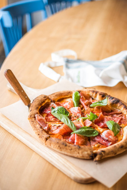 Смачна піца стоїть на столі, піца з червоним соусом, панцета і базил, італійська кухня, піцерія. - Фото, зображення