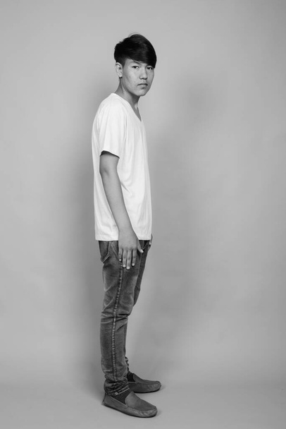 Студийный кадр молодого азиатского подростка на сером фоне в черно-белом - Фото, изображение