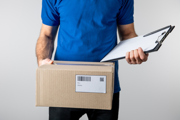 Cropped view of courier holding clipboard and cardboard box isolated on grey - Fotografie, Obrázek