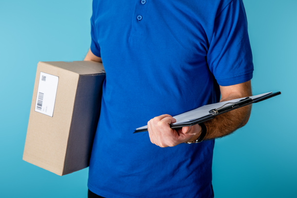 Vista recortada del repartidor sujetando el portapapeles y el paquete de cartón aislado en azul
 - Foto, Imagen