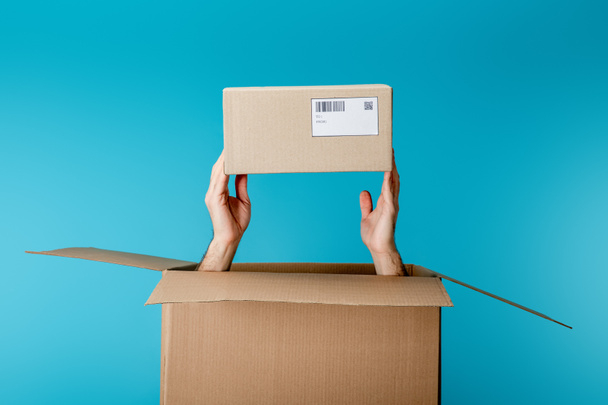 Vista recortada del mensajero que sostiene la caja de cartón del paquete aislado en azul
 - Foto, Imagen