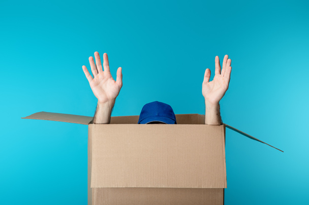 Hands and cap of delivery man in cardboard box isolated on blue - Photo, Image