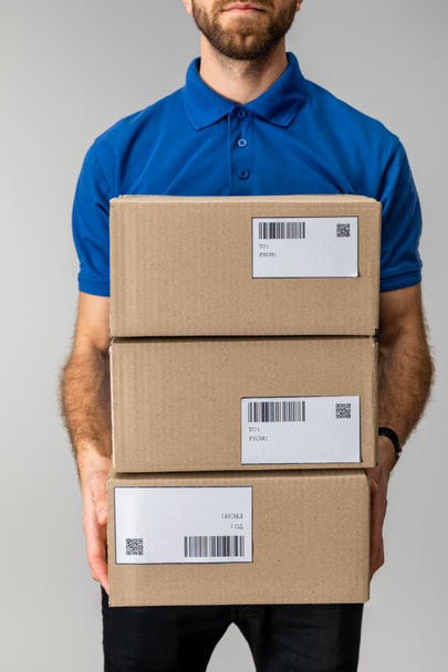 Cropped view of courier holding boxes with barcodes and qr codes isolated on grey - Photo, Image