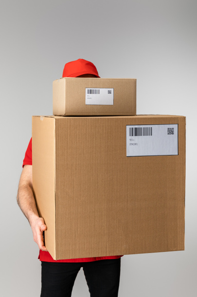 Courier in uniform holding boxes with barcodes and qr codes on cards isolated on grey - Foto, immagini