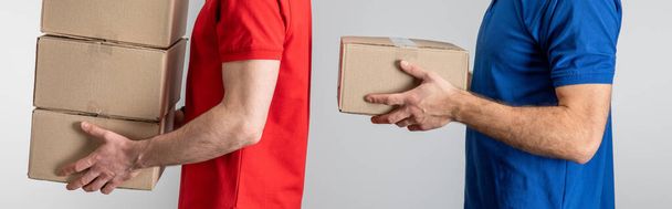 Side view of delivery men holding cardboard packages isolated on grey, panoramic shot - Foto, Imagem