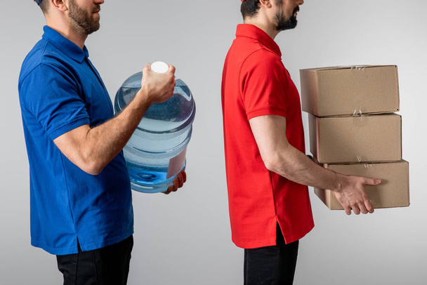 Side view of couriers holding cardboard boxes and bottled water isolated on grey - Photo, Image