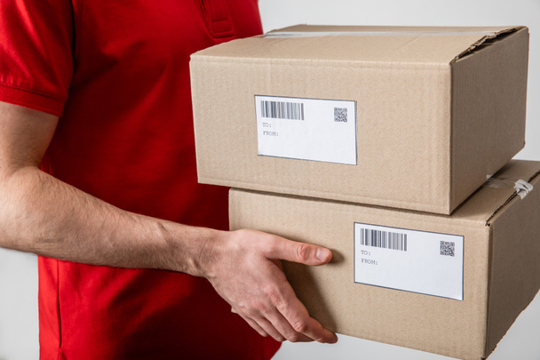 Cropped view of delivery man holding packages with qr codes and barcodes on cards isolated on grey - Foto, Imagem