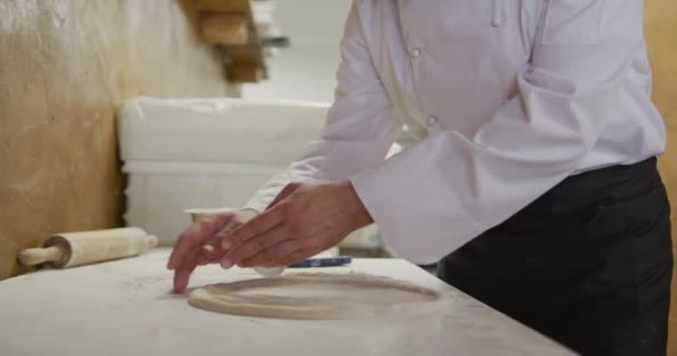 Portrait of a happy Caucasian male chef working in a busy pizza restaurant kitchen, preparing pizza dough before cooking. Busy chefs at work in commercial kitchen. - Video